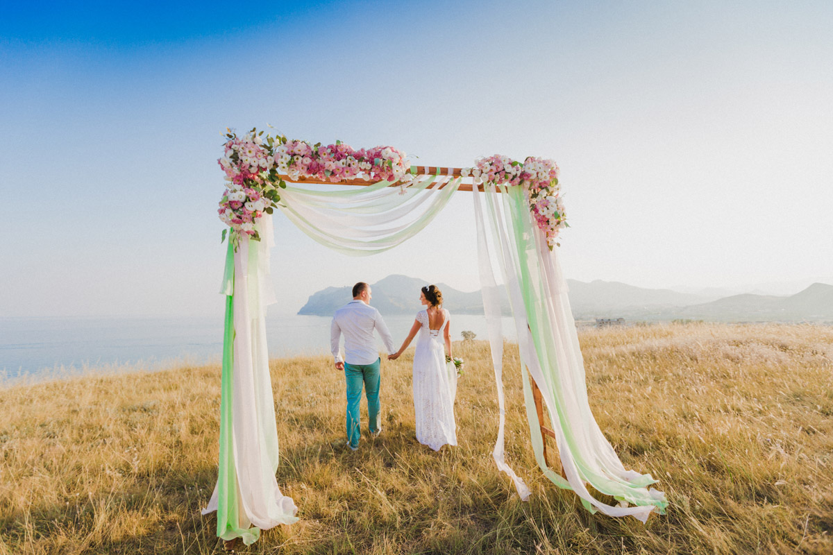 Жених и невеста у свадебной арки на фоне гор и моря